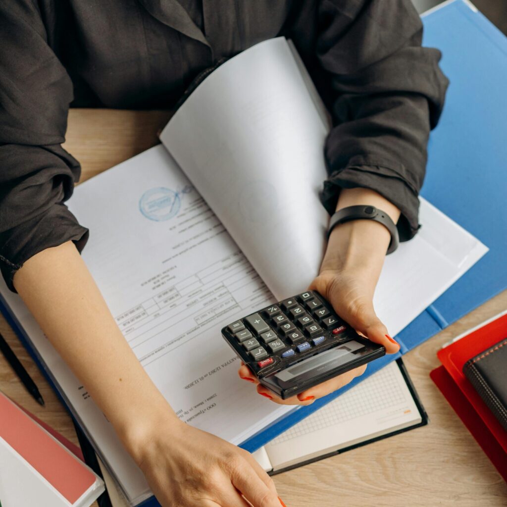 A business professional uses a calculator among documents and laptop on a desk for financial tasks.